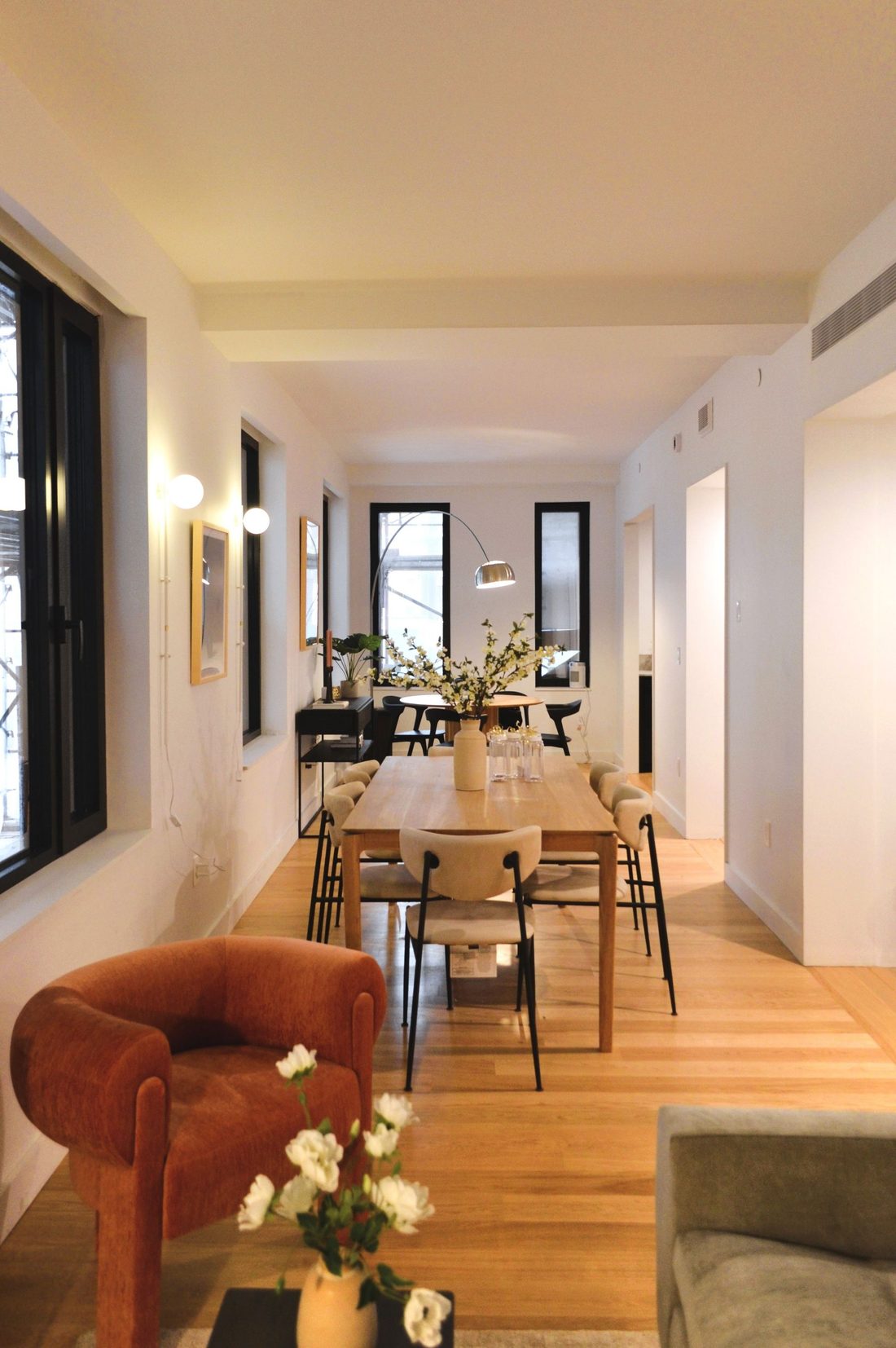Finished apartment interior at 147 St. Felix Street with white oak floors, a long dining table, black-framed windows, and a rust-colored armchair